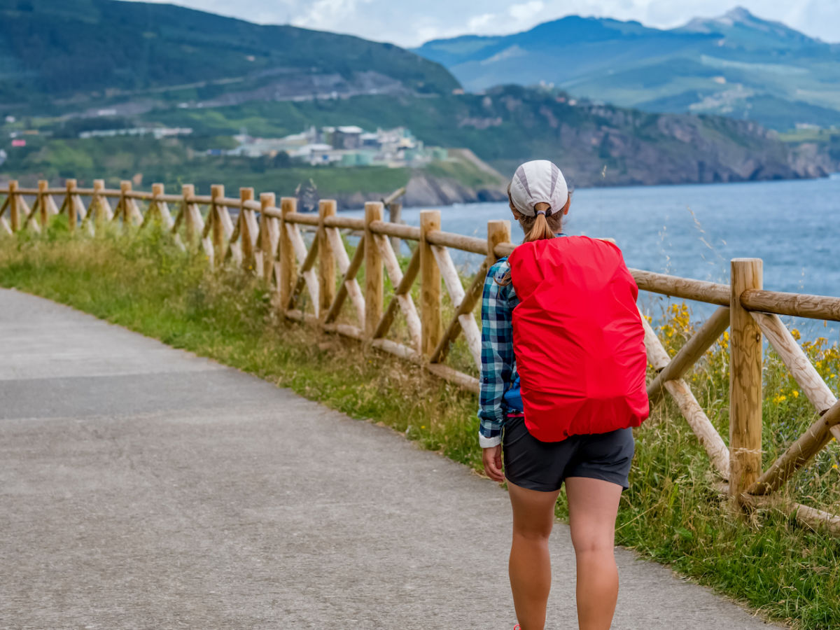 Peregrina con mochila roja en el Camino de Santiago en verano con cielo soleado