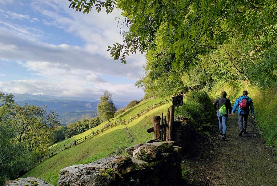 Dos peregrinos caminando por el sendero del Camino Primitivo en Asturias con vistas al valle